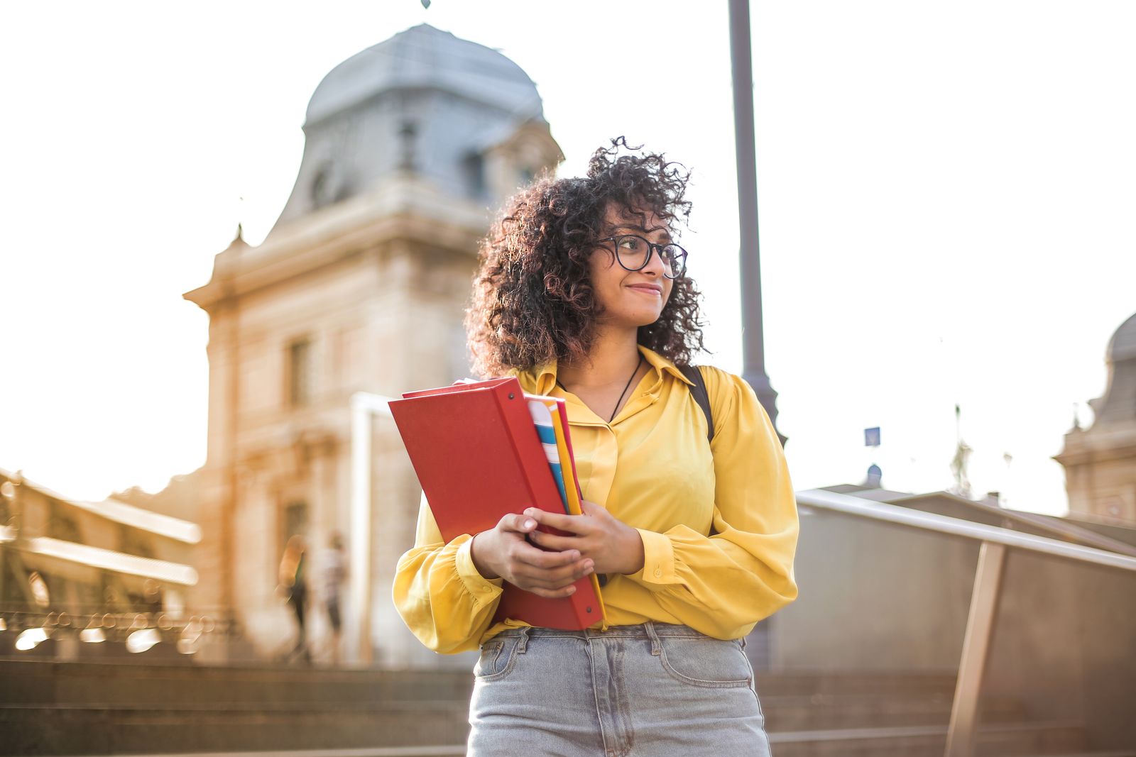 Professora de português com livros na mão em frente a um edifício histórico